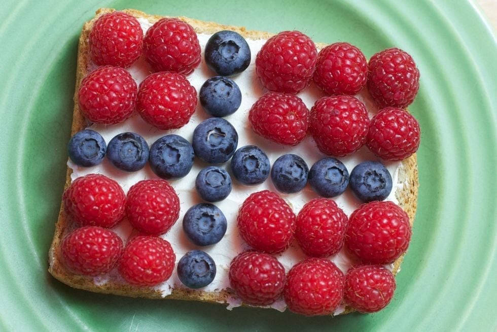 Skive med flaggpynt laget av kremost, bringebær og blåbær