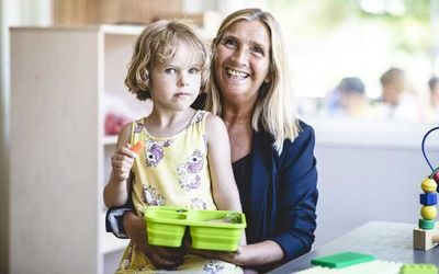 Barnehagebarn med matpakke og barnehagelærer