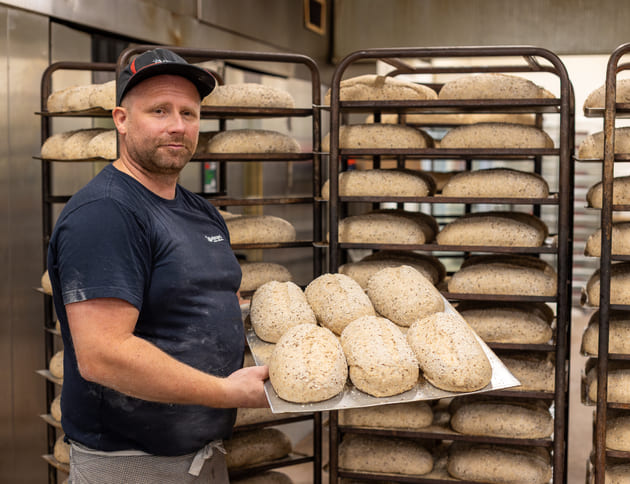 Baker hos Østlyngens Bakeri & Konditori viser frem seks brød laget med norsk korn klare til steking