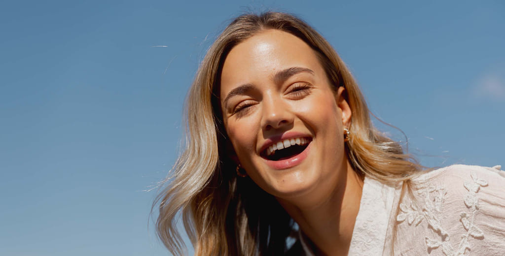 Smilende dame med flott smil mot blå himmel