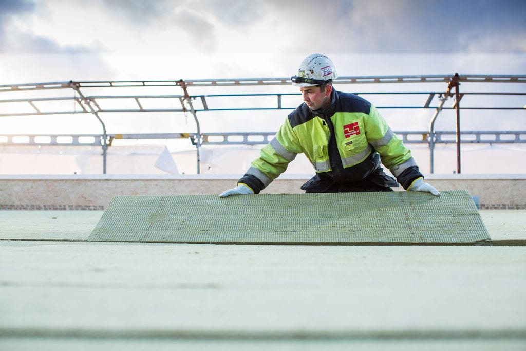 Bygningsarbeider fra Hesselbergtak i verneutstyr som legger isolasjonsplater på et tak.