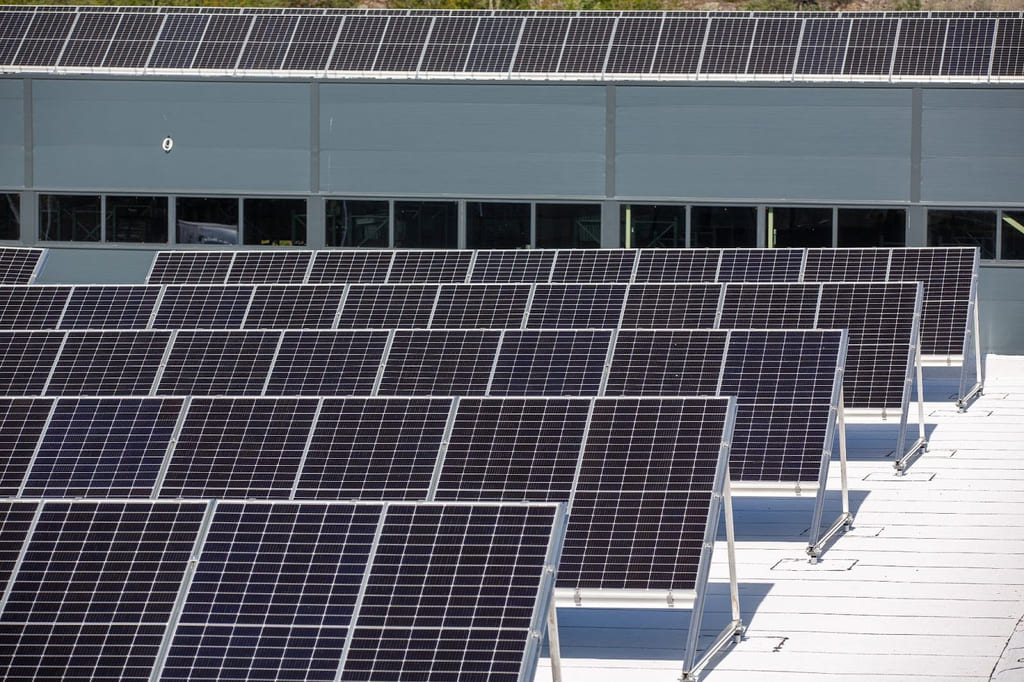 Solcellepaneler montert i flere rader på et flatt tak, med en bygning i bakgrunnen.