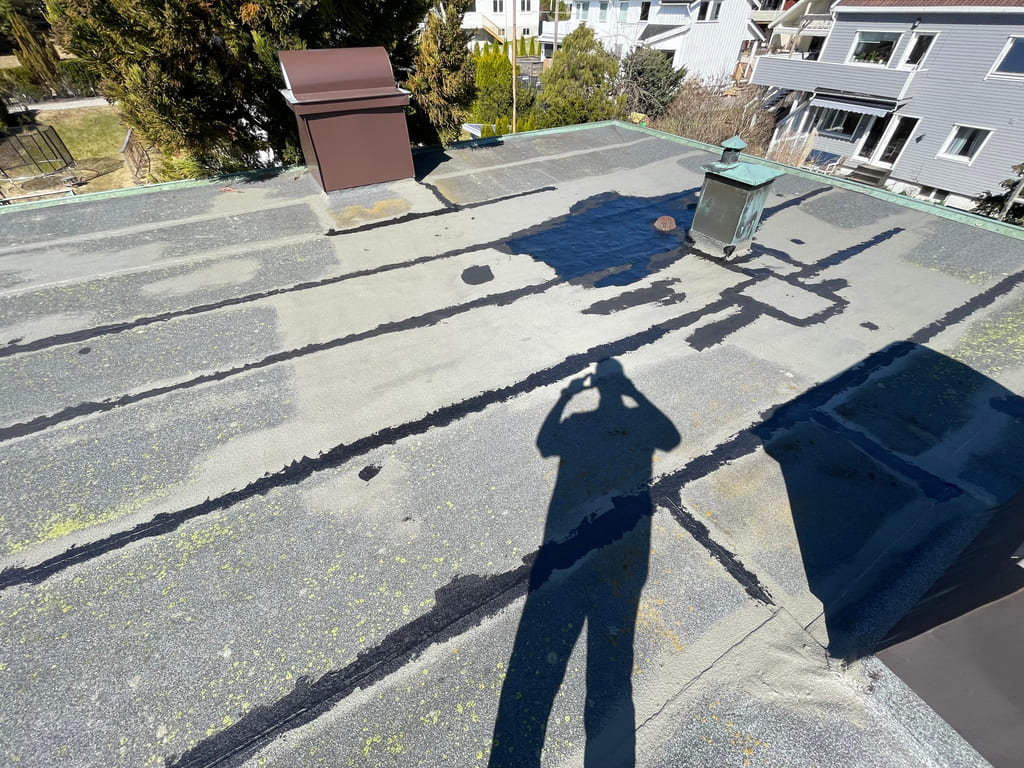 Eldre takflate med lappede partier og tettemasse i flere linjer og overganger.