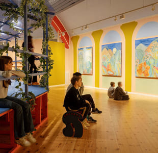 Flere barn sitter i et stort rom og stirrer på veggmalerier.