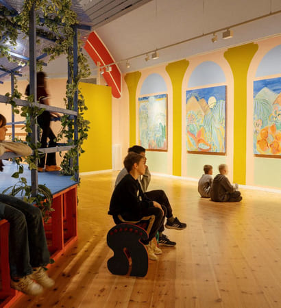 Flere barn sitter i et stort rom og stirrer på veggmalerier.