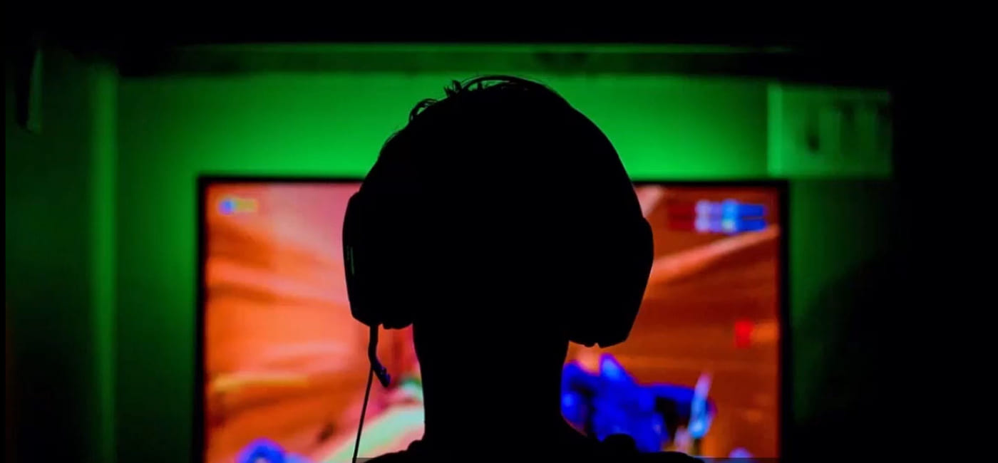 Silhuett av person med hodetelefoner foran en pc-skjerm.