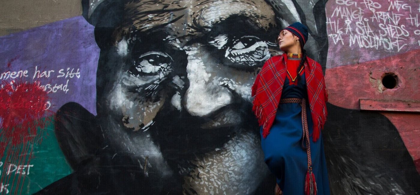 Timimie Märak i samedrakt foran graffitivegg