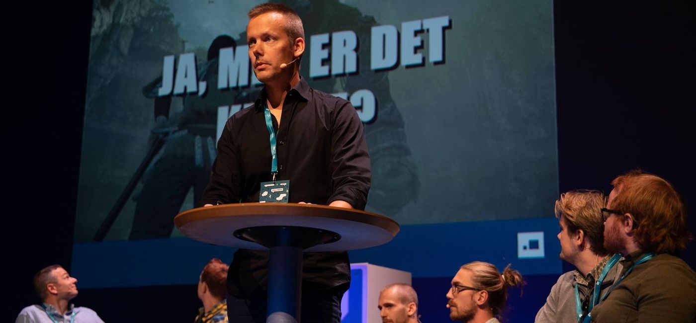 Mann taler på scenen med panel bak seg