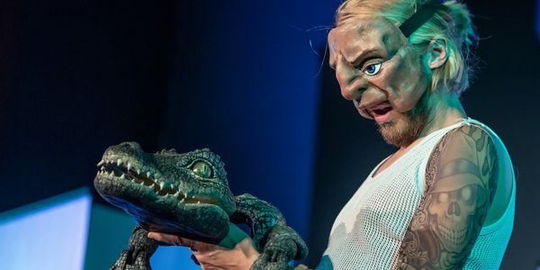 Mann med maske holder en liten alligator-dukke