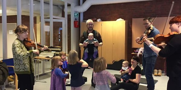 Barn og voksne står i ring. Spiller instrumenter.