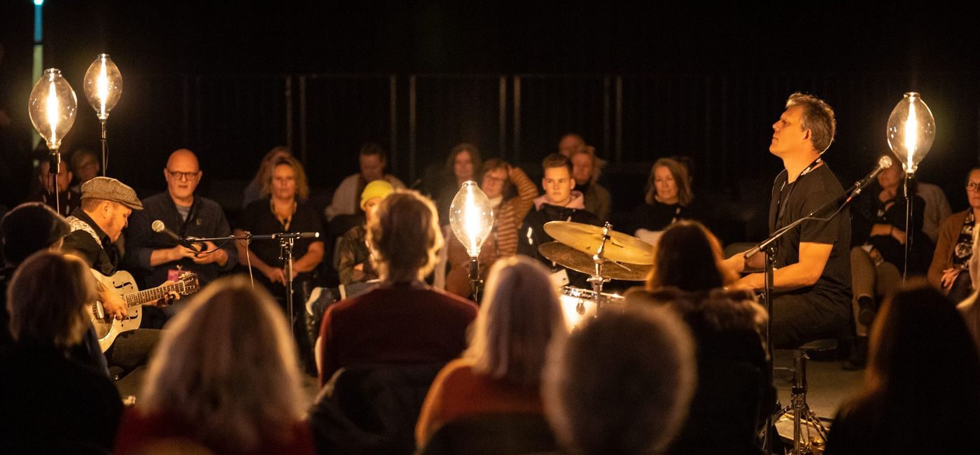 En trommis og en gitarist fremfører for publikum som sitter i ring rundt dem