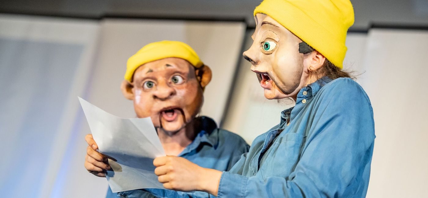 To skuespillere i komiske masker leser fra et ark