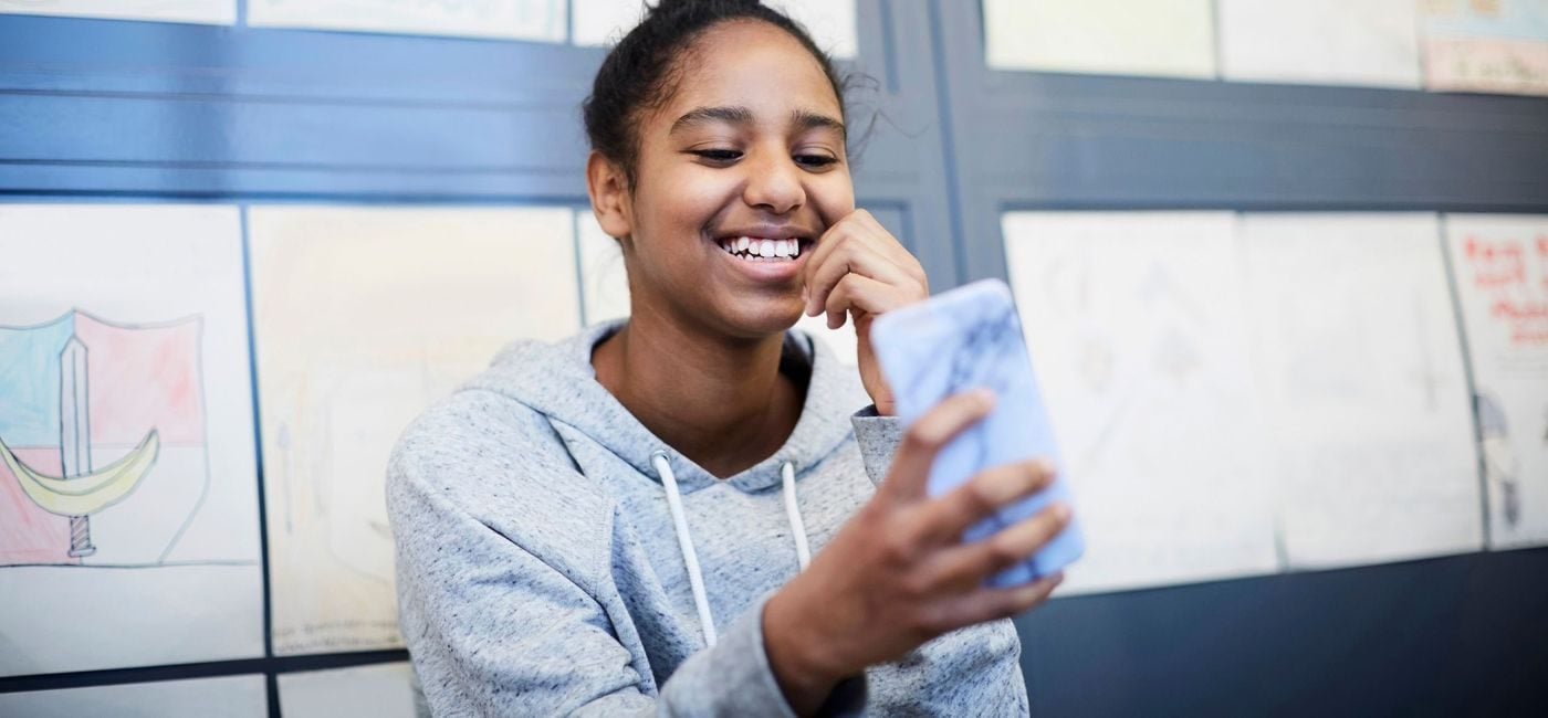 ei jente ser på mobilen, hun smiler