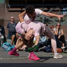 To dansere holder og danser rundt hverandre på en skolegård mens publikum ser på i bakgrunnen