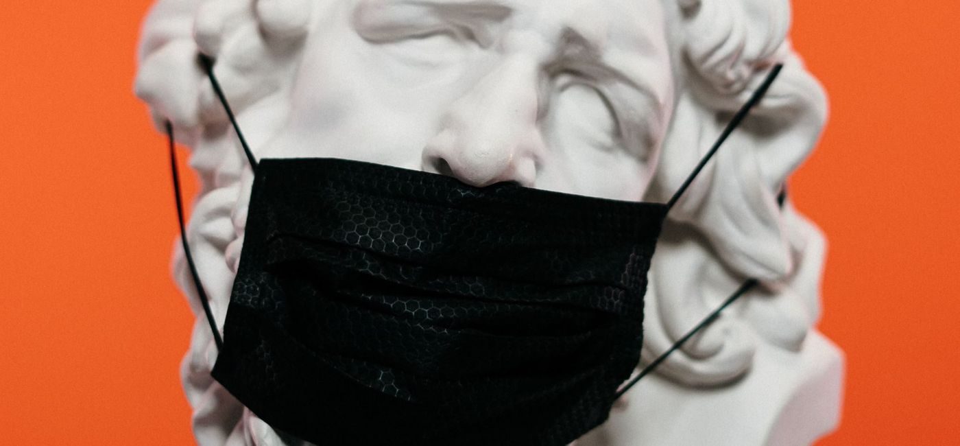 Hvit statue med sort ansiktsmaske foran en oransj vegg