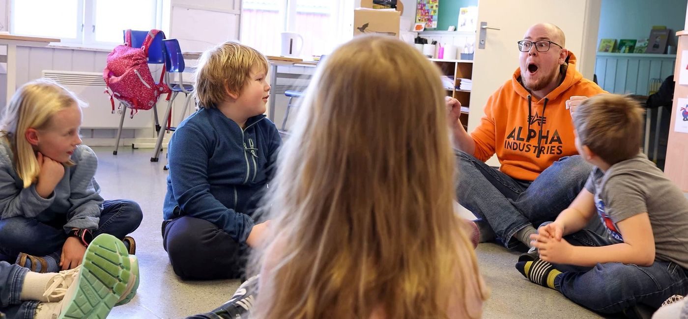 Elever og kunstner sitter på gulvet i klasserommet.