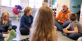 Elever og kunstner sitter på gulvet i klasserommet.