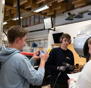 En elev filmer en annen mens en tredje elev ser ned i et ark