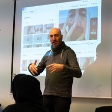 En mann forklarer noe foran en skjerm i et klasserom. På skjermen ser du et bilde av han i nærbilde