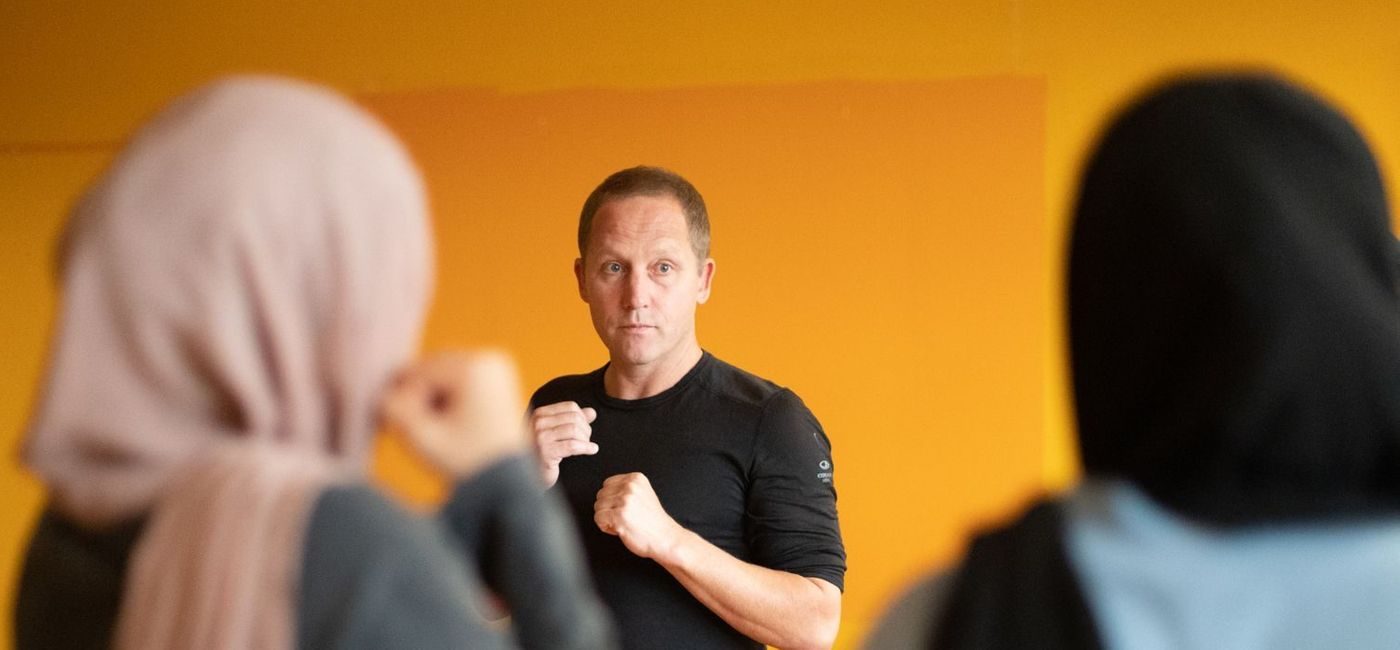 en mann viser hvordan to jenter i hijab skal bokse