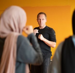 en mann viser hvordan to jenter i hijab skal bokse