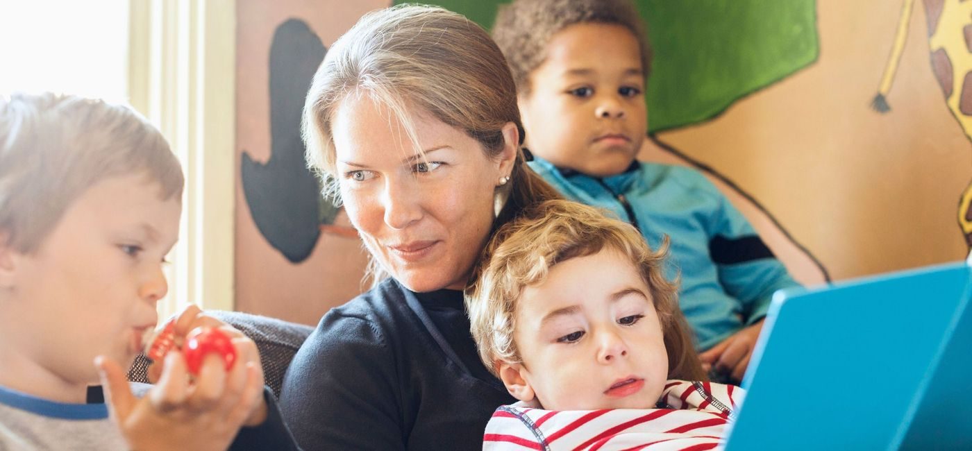 en dame leser fra en bok. Et barn sitter på fanget hennes,et barn sitter på hver side av henne