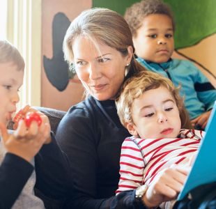 en dame leser fra en bok. Et barn sitter på fanget hennes,et barn sitter på hver side av henne