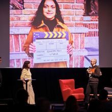 En programleder og to personer står på en scene og presenterer en film for publikum