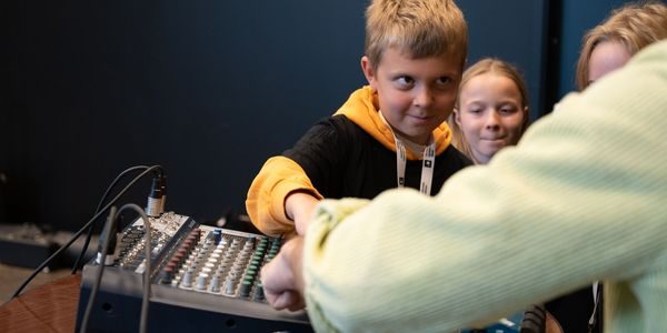 en elev tar på et lydbord og ser opp. Ei jente smiler i bakgrunnen