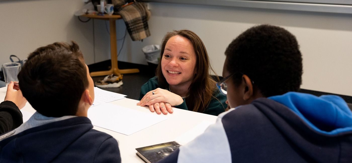 Forfatter Mari Moen Holsve sitter på huk foran en pult og prater til to elever.