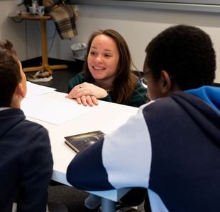 Forfatter Mari Moen Holsve sitter på huk foran en pult og prater til to elever.