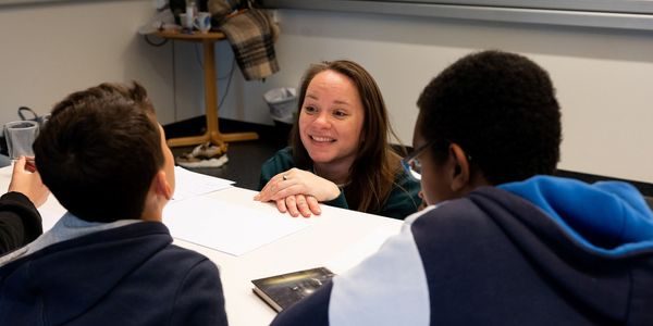 Forfatter Mari Moen Holsve sitter på huk foran en pult og prater til to elever.