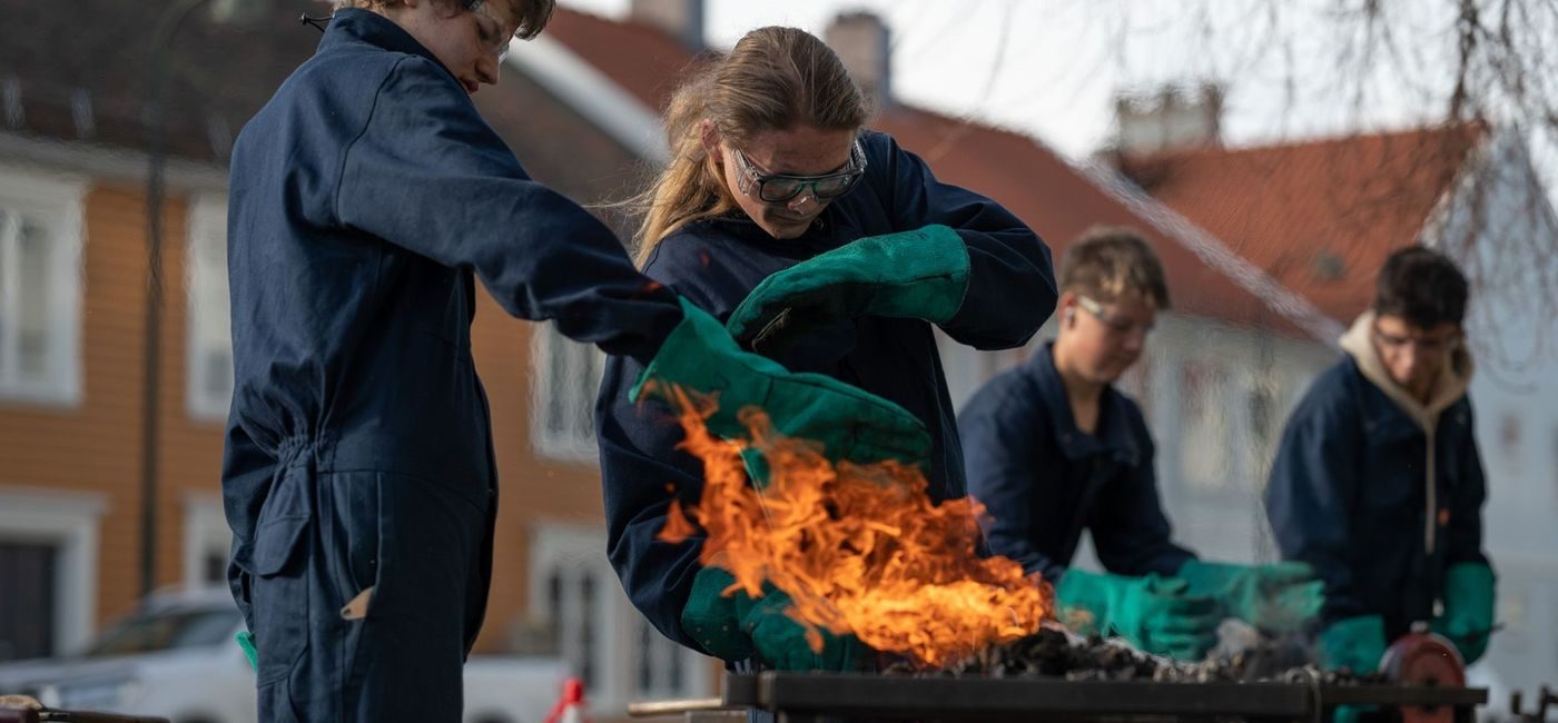 Elever skjermer seg mot flammer som stiger opp mot dem. De har på seg verneutstyr