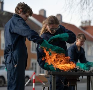 Elever skjermer seg mot flammer som stiger opp mot dem. De har på seg verneutstyr