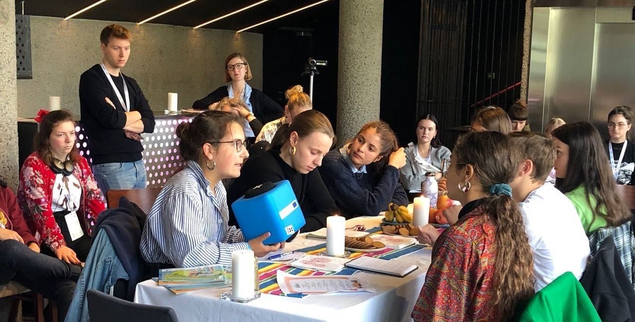 Deltakere sitter rundt et bord. en holder en blå firkant.