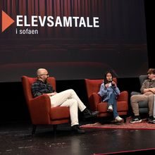 På en scene sitter en mann i en godstol og prater med fire ungdommer. En ungdom sitter også i en godstol mens de andre sitter i en sofa ved siden av stolene. På storskjerm bak dem står det "Elevsamtale i sofaen".