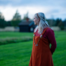 Kvinne i vikingdrakt ser ut over en grønn eng.