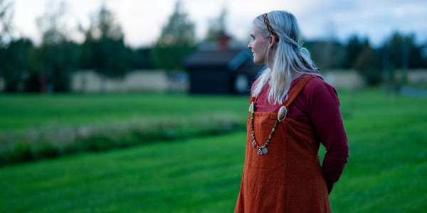 Kvinne i vikingdrakt ser ut over en grønn eng.