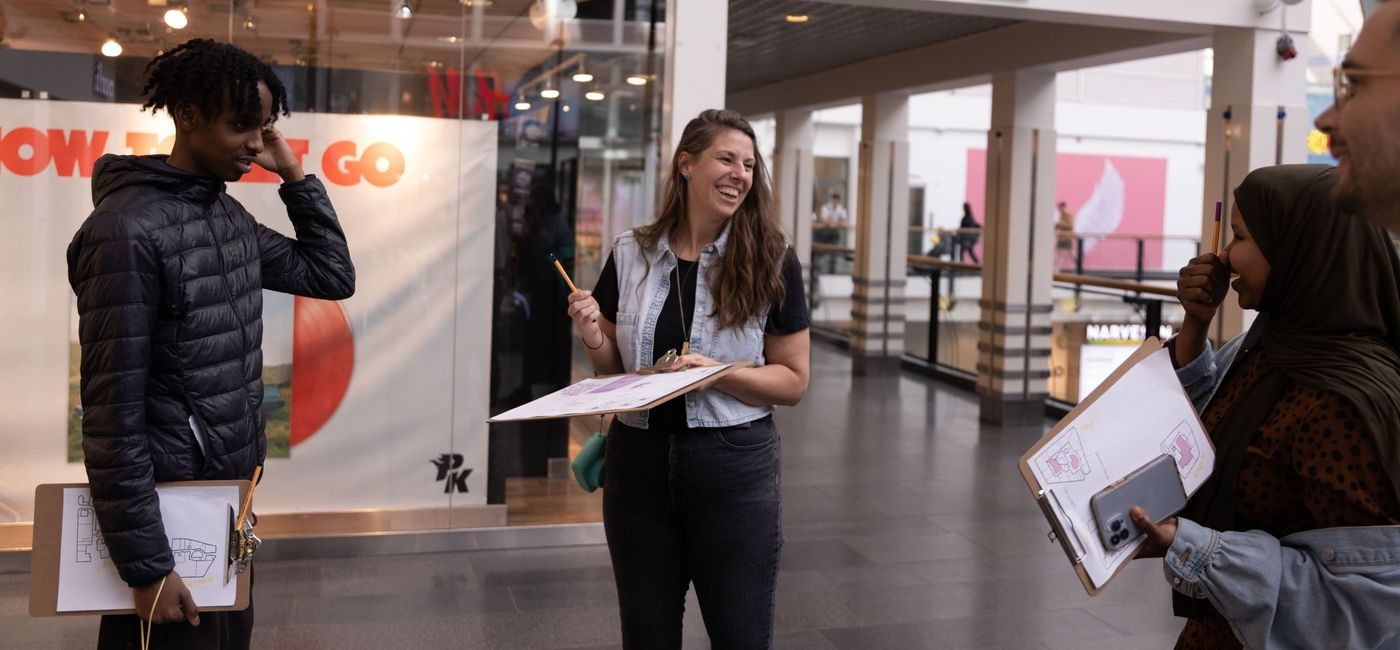 En kvinne og to ungdommer smiler, de står inne på et kjøpesenter med hver sin skriveplate i hendene.