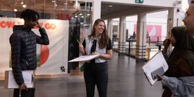 En kvinne og to ungdommer smiler, de står inne på et kjøpesenter med hver sin skriveplate i hendene.