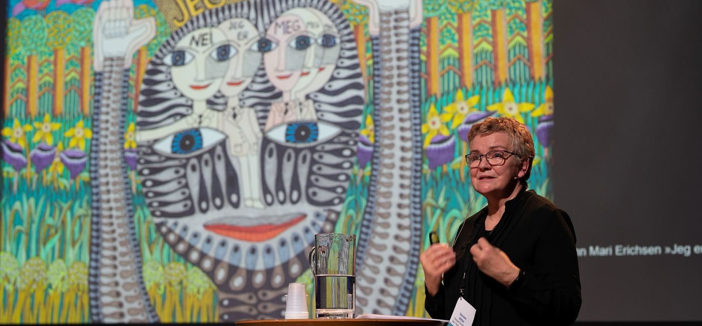 en dame kledd i sort står foran et fargerikt bilde