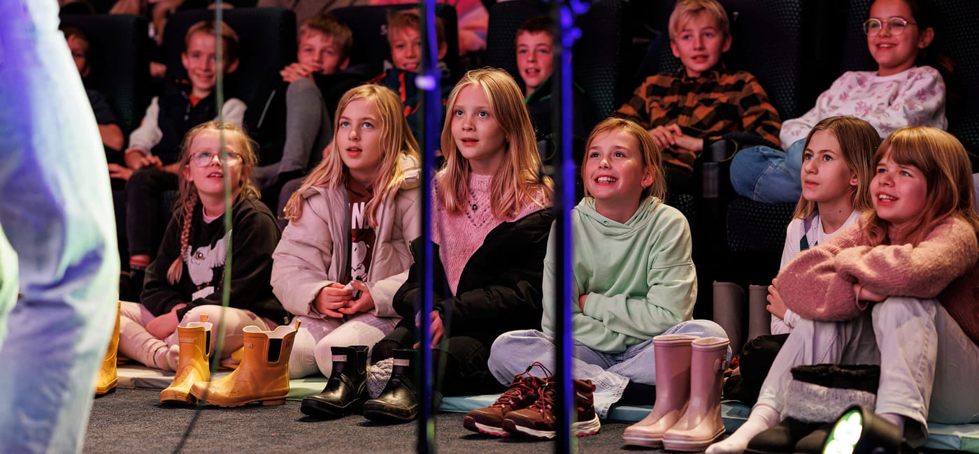 Smilende elever ser på utøver i forgrunnen.