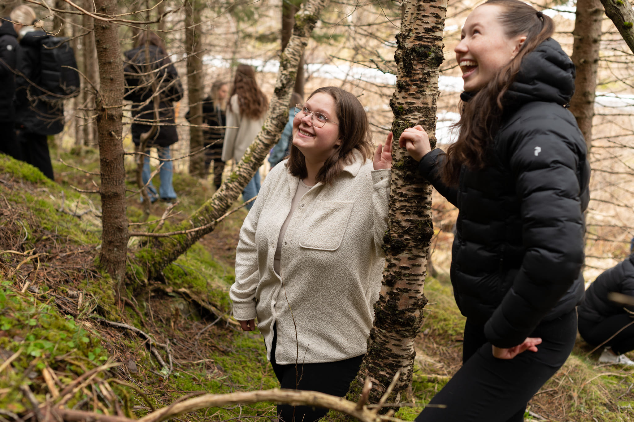 To unge kvinner ser på noe. Begge smiler. De står i en skog.