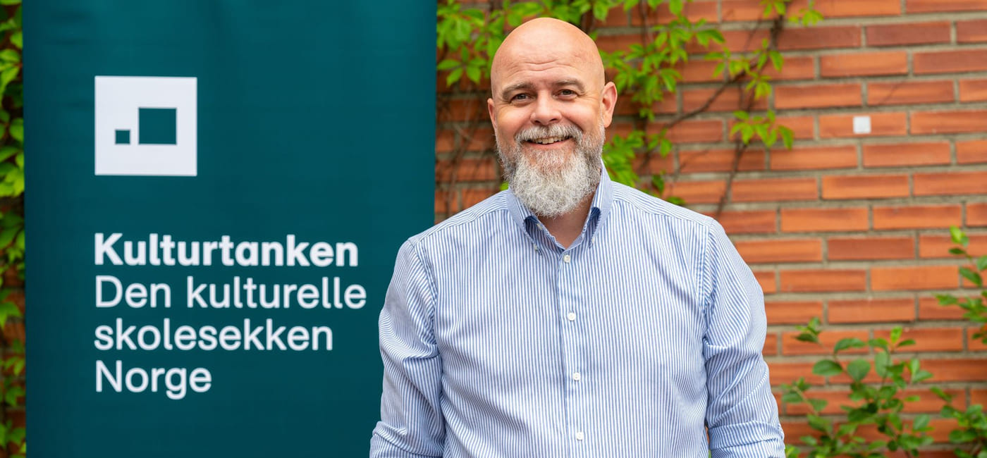Matias Hilmar Iversen foran et skilt hvor det står Kulturtanken - Den kulturelle skolesekken Norge