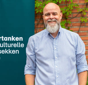 Matias Hilmar Iversen foran et skilt hvor det står Kulturtanken - Den kulturelle skolesekken Norge