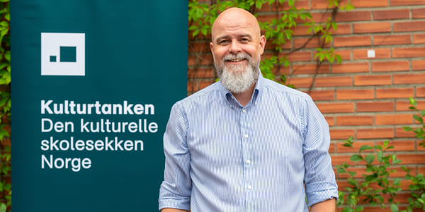 Matias Hilmar Iversen foran et skilt hvor det står Kulturtanken - Den kulturelle skolesekken Norge