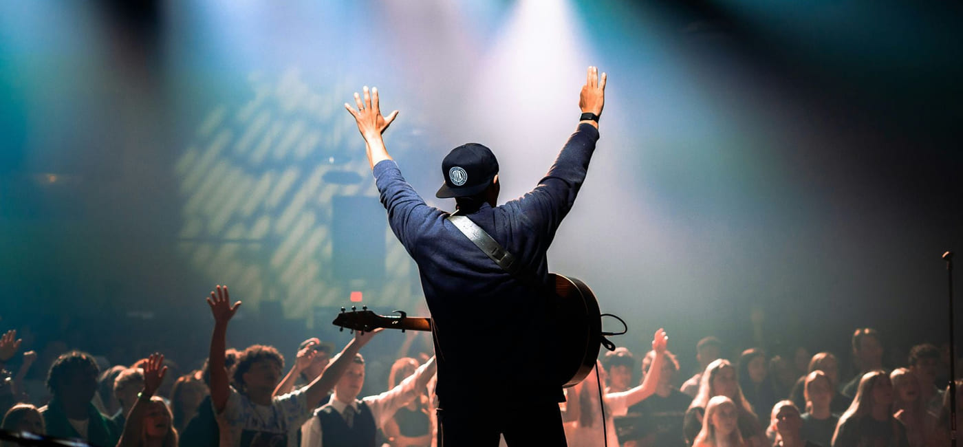 en mann står foran publikum. Han holder hendene i været.