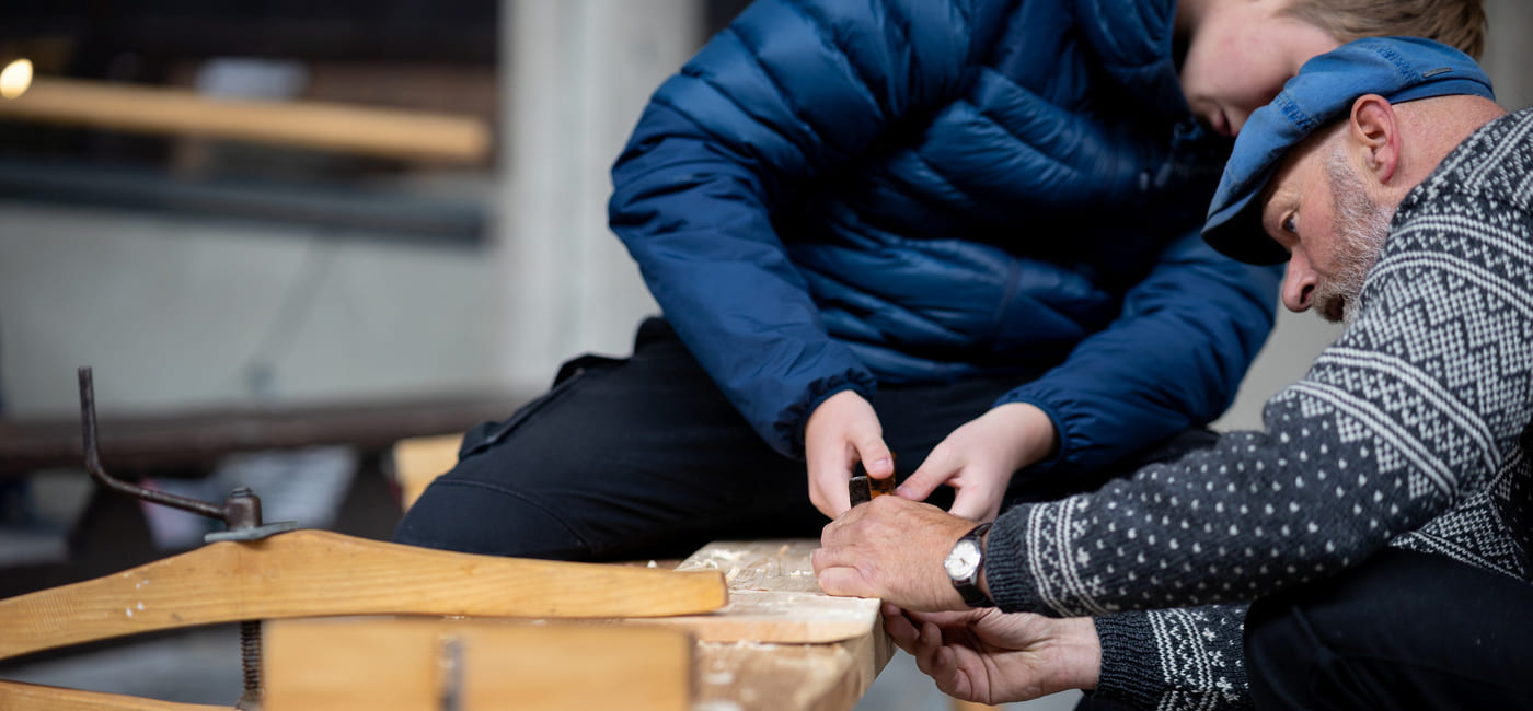 En gutt og en mann samarbeider om å bruke verktøy for å slipe treverk