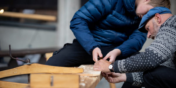 En gutt og en mann samarbeider om å bruke verktøy for å slipe treverk