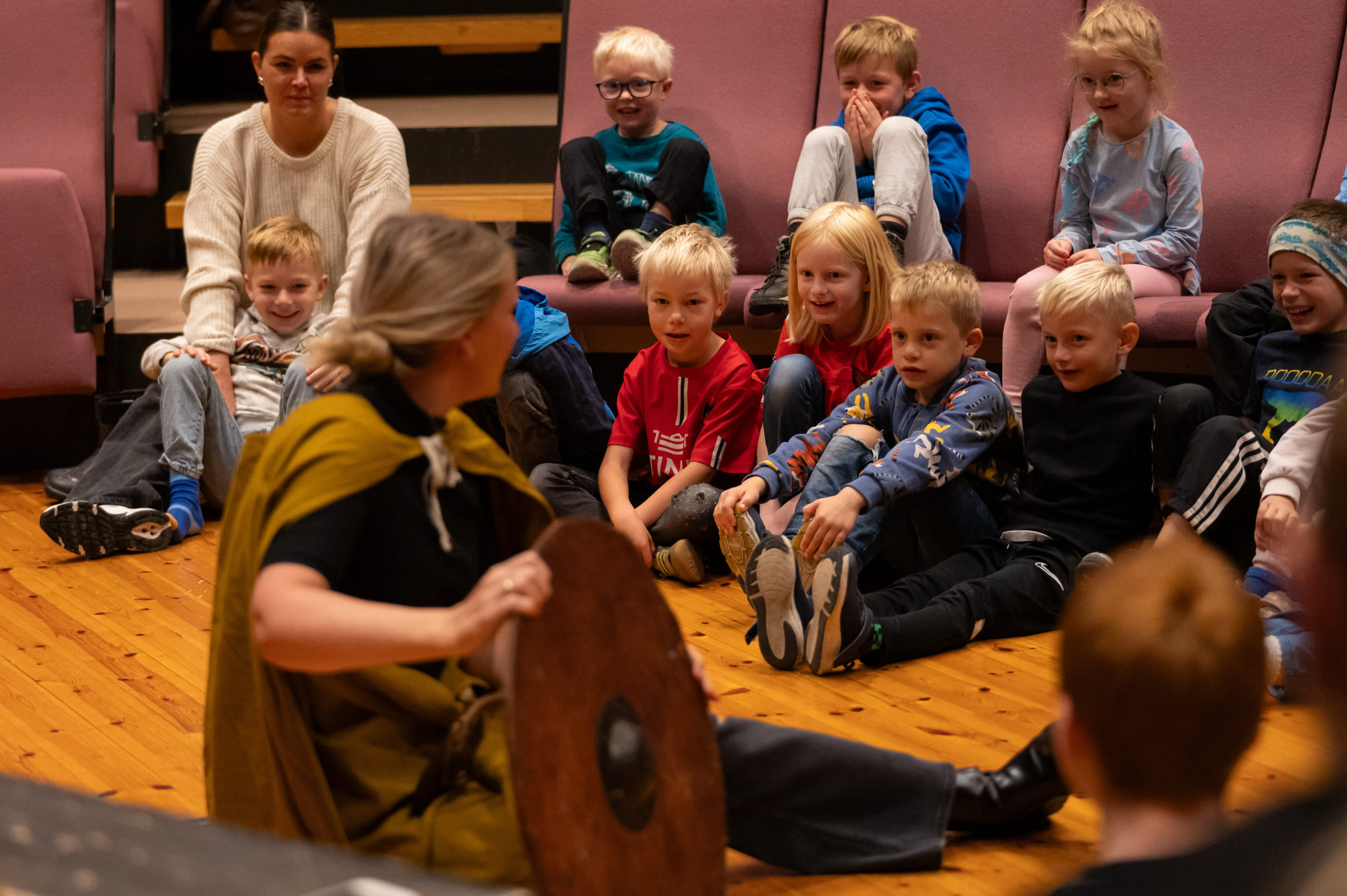En gruppe barn sitter på gulvet og følger med mens en person viser frem historiske gjenstander.
